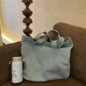 Detail of light blue denim tote with Less Mondays More Sundays embroidery on a sofa