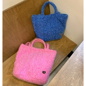 Fuzzy faux fur tote bags in sky blue and bright pink shown on a wooden bench