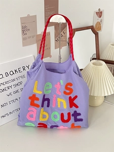 Detail of purple canvas tote bag featuring colorful embroidered text and red rope handles