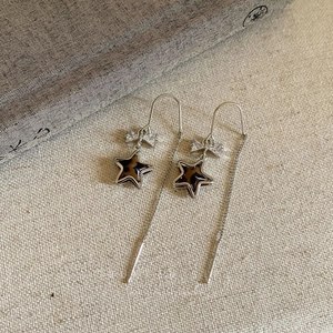 Detail of silver bow long chain earrings with leopard print star charms on beige linen