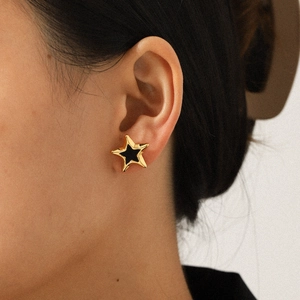Gold stainless steel star stud earrings with black enamel inlay on a female model