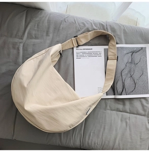 Flat lay of a beige nylon crescent crossbody bag with adjustable strap on a gray background