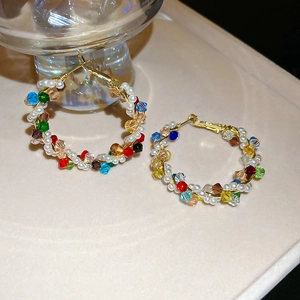 Close-up of golden metal hoop earrings with woven colorful crystals and white pearls