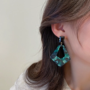 Detail of geometric acrylic earrings with green diamond pattern on an elegant model