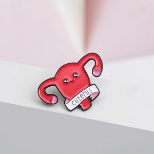 Macro shot of creative Cuterus enamel pin with red uterus shape and slogan