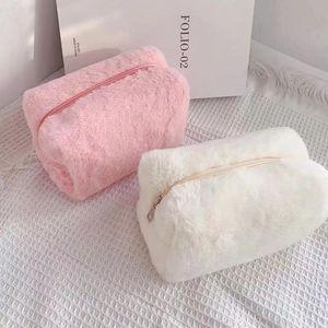 Close-up of soft plush macaron-colored makeup bags in pink and white with gold zipper details