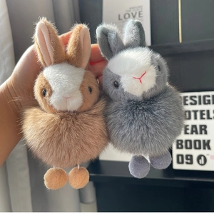 Close-up of soft plush rabbit keychains in brown and grey held in hand with fluffy fur texture