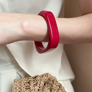 Macro shot of a bold red acrylic resin bangle on model wrist for a retro fashion look