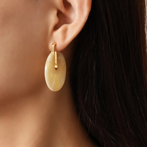 Detail of 18K gold-plated oval acetate earrings in cream beige on a model