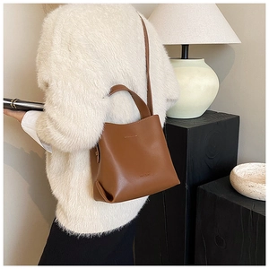 Brown leather bucket bag with top handle and shoulder strap shown in a cozy indoor setting
