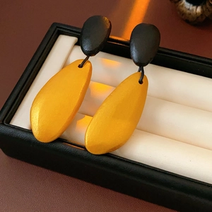 Detail view of yellow teardrop wood earrings with black tops on white jewelry cushion