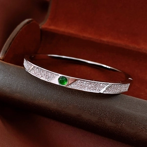 Macro shot of silver metal bangle featuring a central round green gemstone and pavé zircons