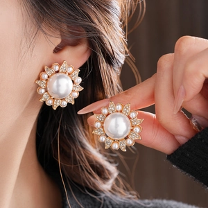 Close-up of model wearing floral pearl stud earrings with crystal halo and gold finish