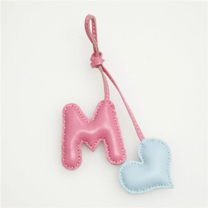 Close-up of pink leather letter M charm with blue heart and white stitching detail