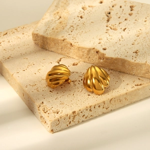 Détail macro de boucles d'oreilles coquillage doré sur pierres de travertin beige