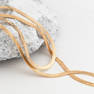 Detail of flat golden snake chain necklace on white stone with polished metallic texture