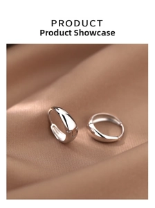 Macro shot of polished silver teardrop hoop earrings on elegant brown satin fabric
