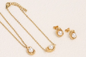 Detail showing elegant pearl stud earrings and gold pea-shaped necklace on beige texture