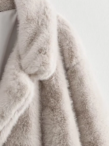 Détail d'un manteau en fausse fourrure gris clair montrant le col doux et l'épaule