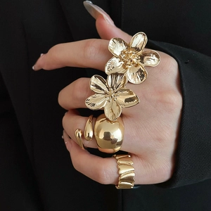 Close-up of gold flower rings and irregular thick bands worn on fingers over black fabric