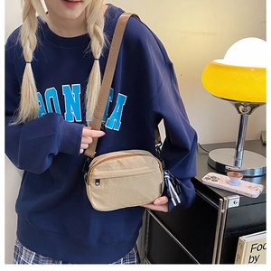 Détail d'un sac bandoulière en nylon beige avec sangle réglable et tirette décorative