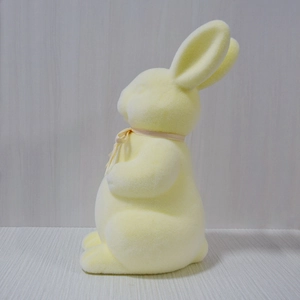 Detail of yellow flocked Easter bunny ornament with ribbon on a textured surface
