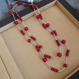 Detail of long layered necklace featuring red round beads and silver metal chain accents