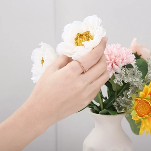 Detail of a 2mm rose gold twisted rope ring on finger with white floral background