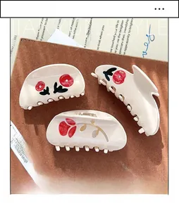 Detailed macro view of cream resin hair claws with embossed red floral rose patterns