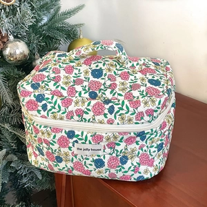 Quilted floral makeup bag with top handle and vintage flower pattern on wooden table