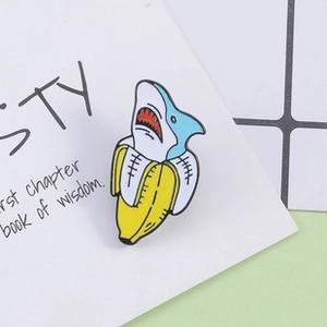 Close-up of a creative cartoon shark banana enamel pin on a white decorative card
