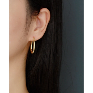 Close-up of minimalist hollow tube golden hoop earring worn by a model for size