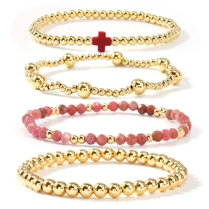 Stacked set of four gold beaded bracelets with a red cross charm and pink crystal beads