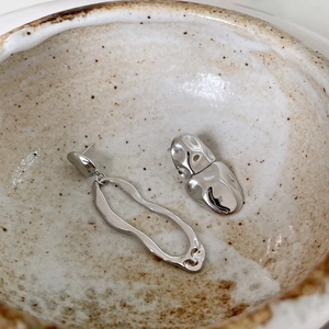 Macro view of 925 sterling silver asymmetric liquid metal earrings in a ceramic bowl