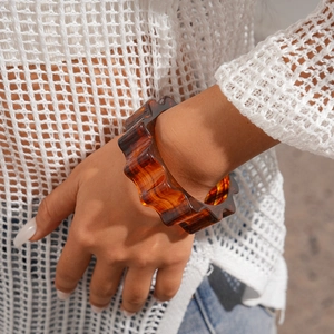 Close-up of model wearing an amber acrylic gear-shaped wide bangle with wavy resin texture