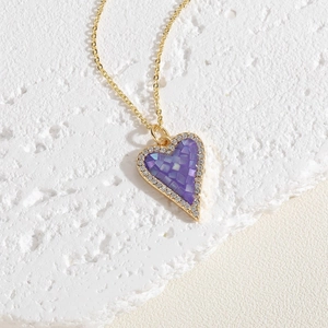 Close-up of golden heart pendant with purple shell mosaic and zircon border on stone base