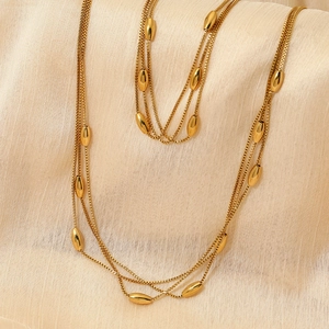 Collier multi-rangs en acier inoxydable doré avec perles ovales sur tissu texturé beige