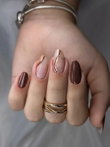Detail of long press-on nails with brown and beige colors, gold lines and glitter
