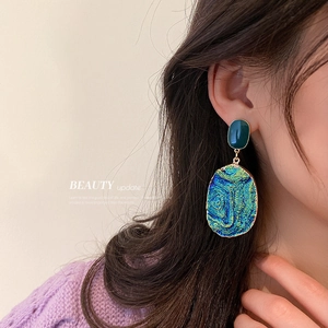Woman wearing blue heart-shaped geometric drop earrings with gold edges and green stones