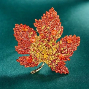 Macro shot of maple leaf brooch with orange and yellow crystals on green velvet