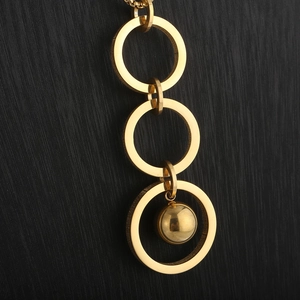 Detail of interlocking triple rings with ball pendant on a gold long tassel necklace