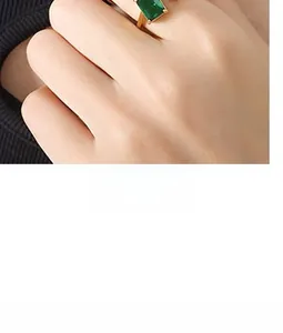 Detailed close-up of a K-gold ring featuring a green emerald-cut gemstone on a model's hand
