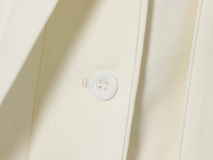 Dettaglio macro del blazer in tessuto crema con cuciture fini e bottone a quattro fori