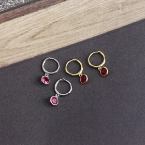 Detail of silver and gold hoop earrings with round red zircon pendants on textured background