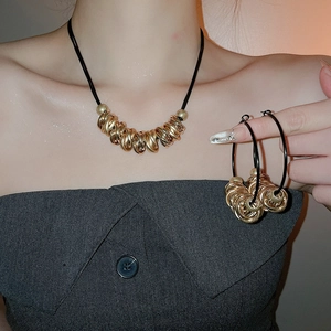 Detail view of gold twisted ring necklace and hoop earrings on a black leather cord