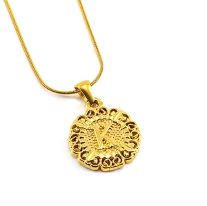 Macro d'un pendentif doré rond avec lettre K ajourée et gravures au style vintage
