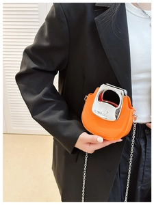 Detail of a mini orange crossbody bag with a silver round handle and chain strap