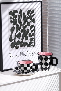 Artistic close-up of handmade checkered ceramic tea set with pink interior on a white surface