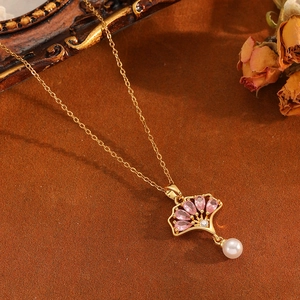 Parure de bijoux ginkgo dorée avec pierres roses et perles blanches sur fond brun