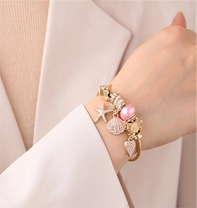 Detail of gold beaded bracelet with pink starfish and shell charms on model wrist